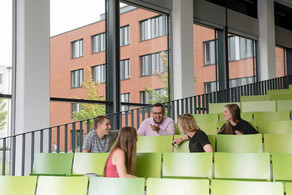 Fünf Studierende sitzen in einem Hörsaal und unterhalten sich.